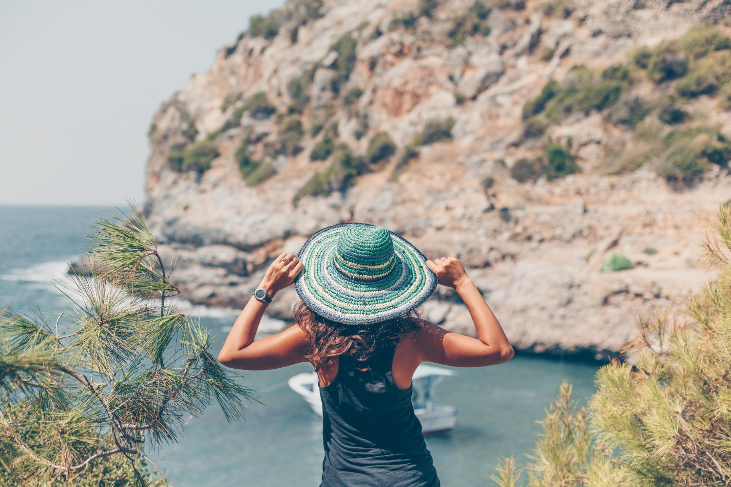 Femme regardant le paysage en tenant son chapeau en bord de mer 